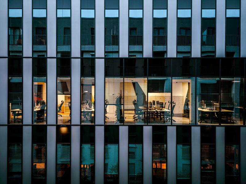Beleuchtete Büroetage hinter einer Glasfassade am Abend, Arbeitsplätze nach Feierabend bereit für die Büroreinigung in Berlin